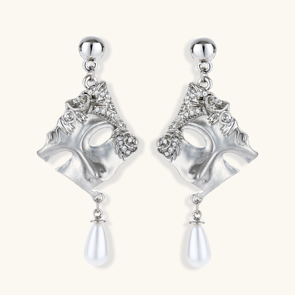 Ornate silver-toned theatrical mask earrings with crystal details and pearl drops on white background.