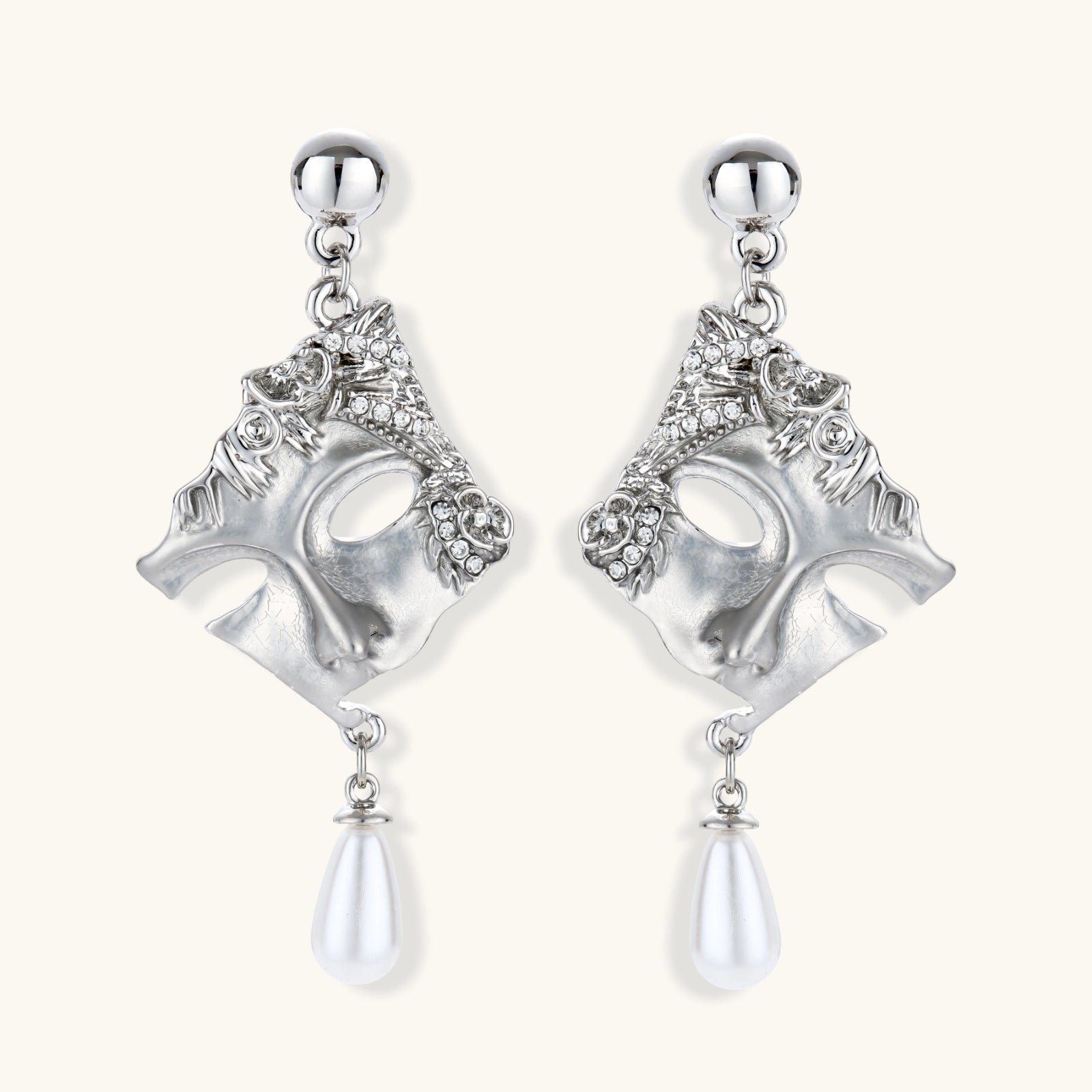 Ornate silver-toned theatrical mask earrings with crystal details and pearl drops on white background.