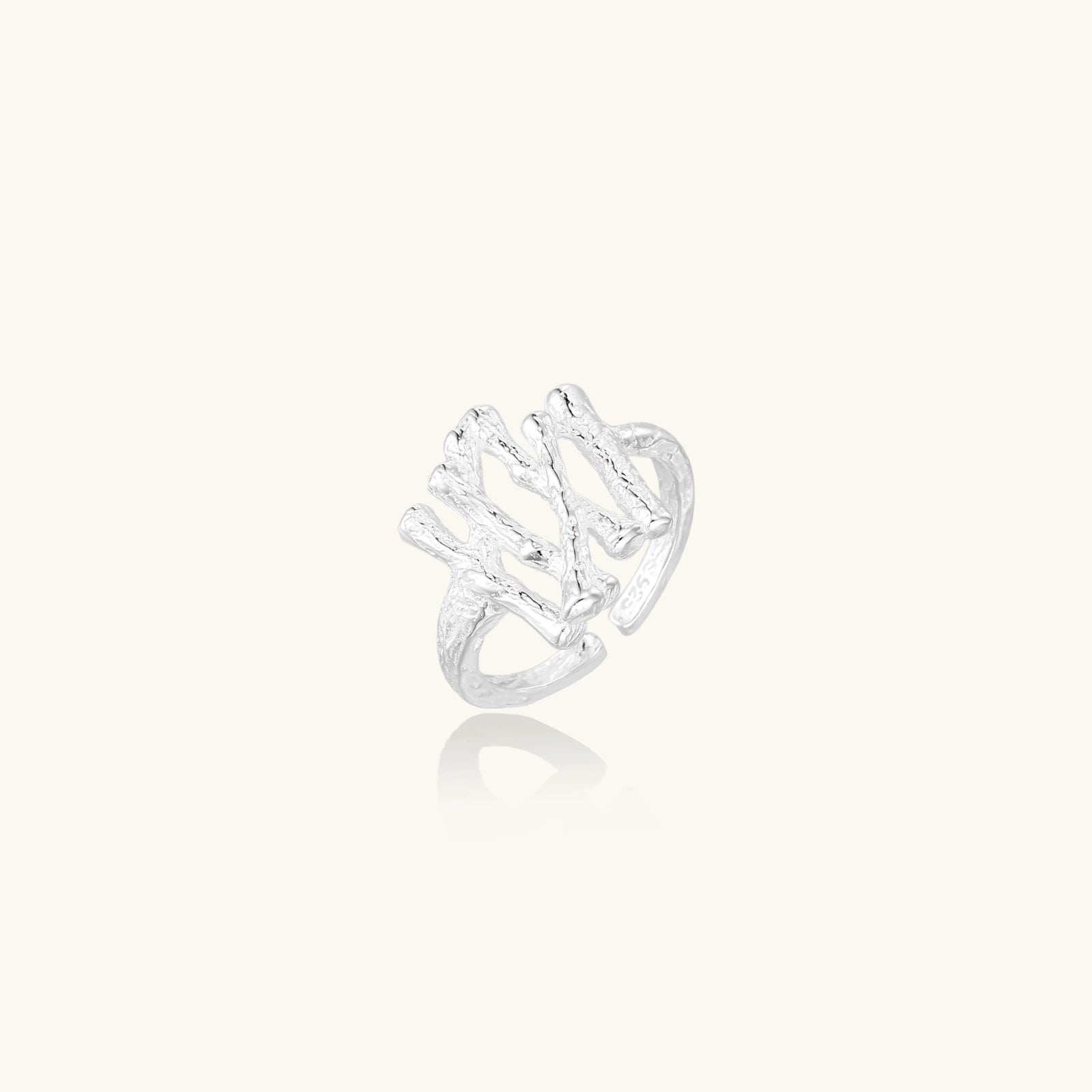 Sculptural sterling silver ring with organic branch design and textured surfaces on cream background