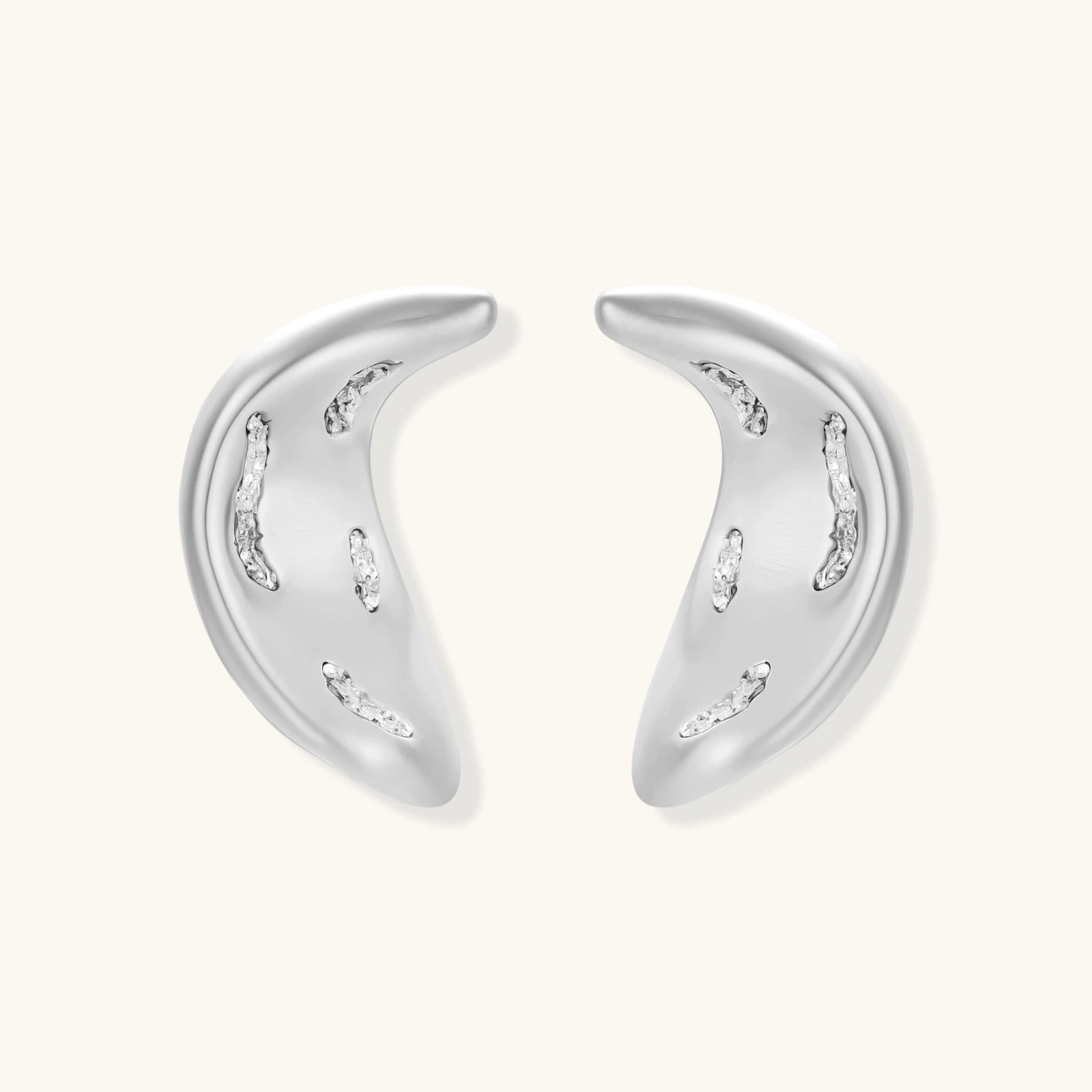 Curved crescent-shaped earrings in gold and silver with scattered perforated details on neutral background.